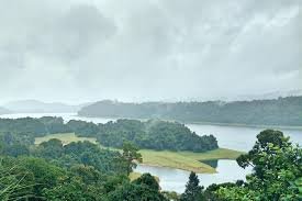 A wide-angle shot of the Sholayar Dam reservoir with deep blue water and lush green forest borders